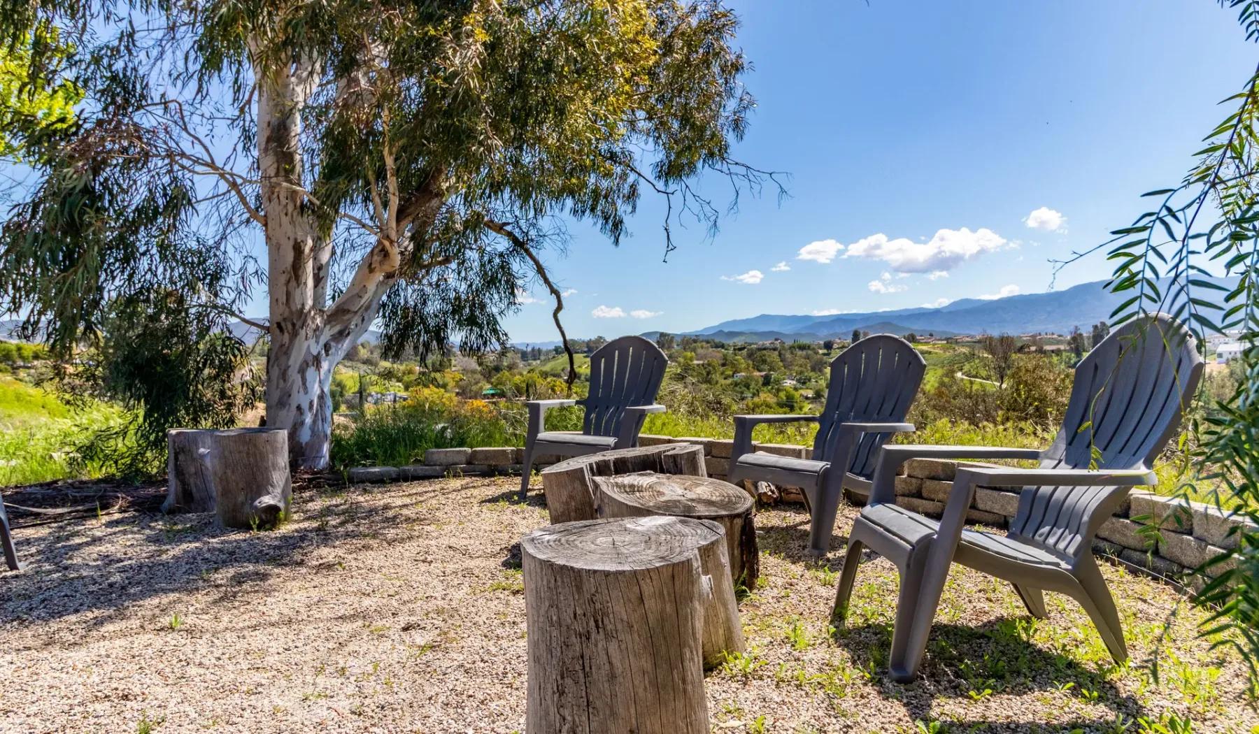 An outdoor seating area with stump tables overlooks a green landscape and distant hills.