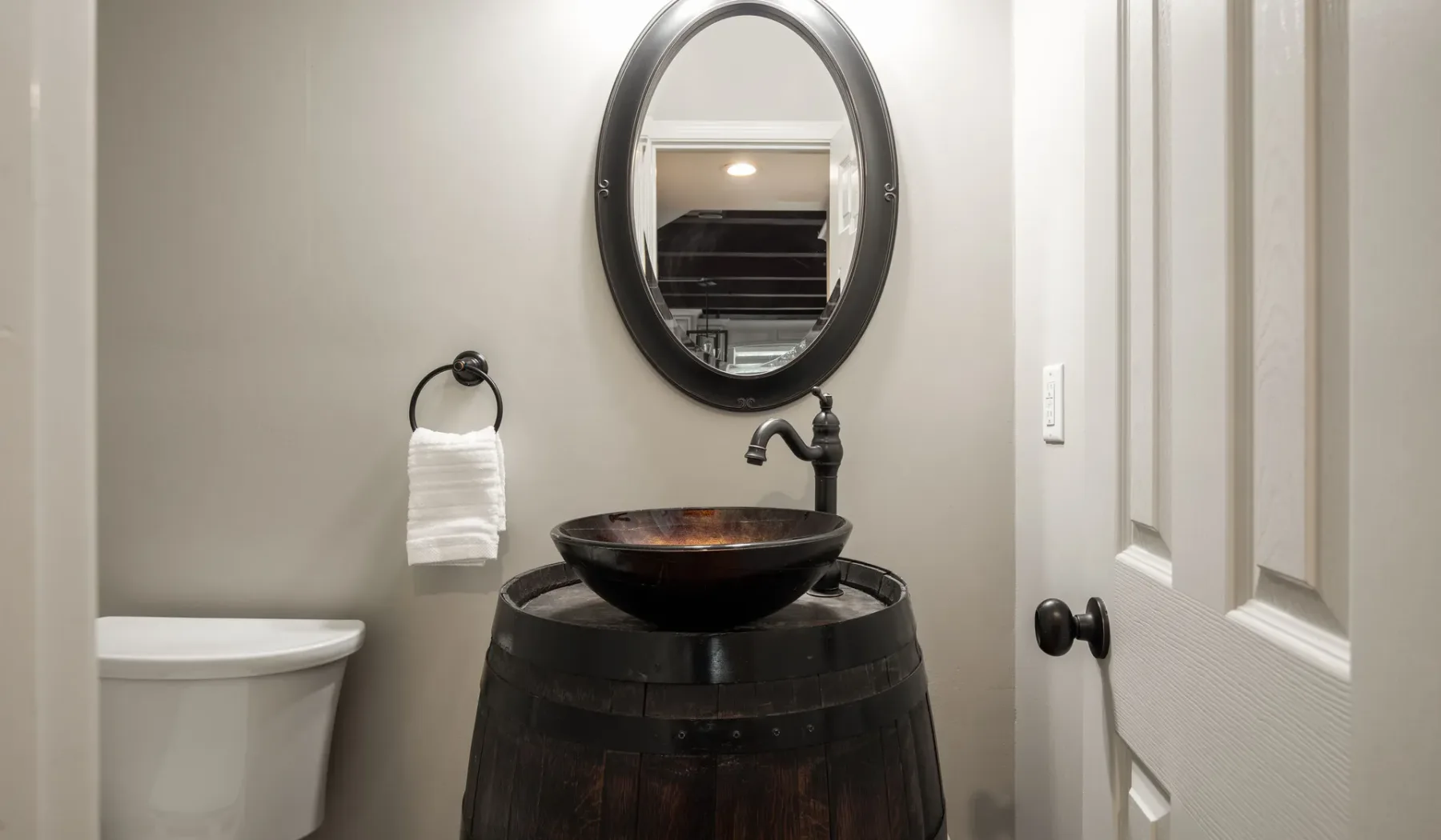 A bathroom vanity features a dark vessel sink beneath an oval mirror.