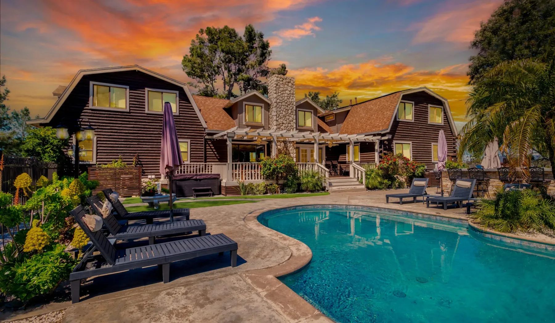 A swimming pool and outdoor seating sit in front of a lodge at sunset.