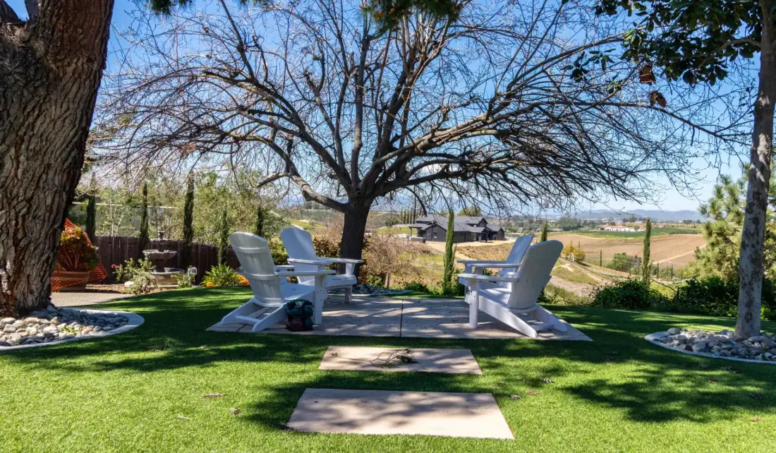 An outdoor seating area beneath a large tree overlooks open fields.