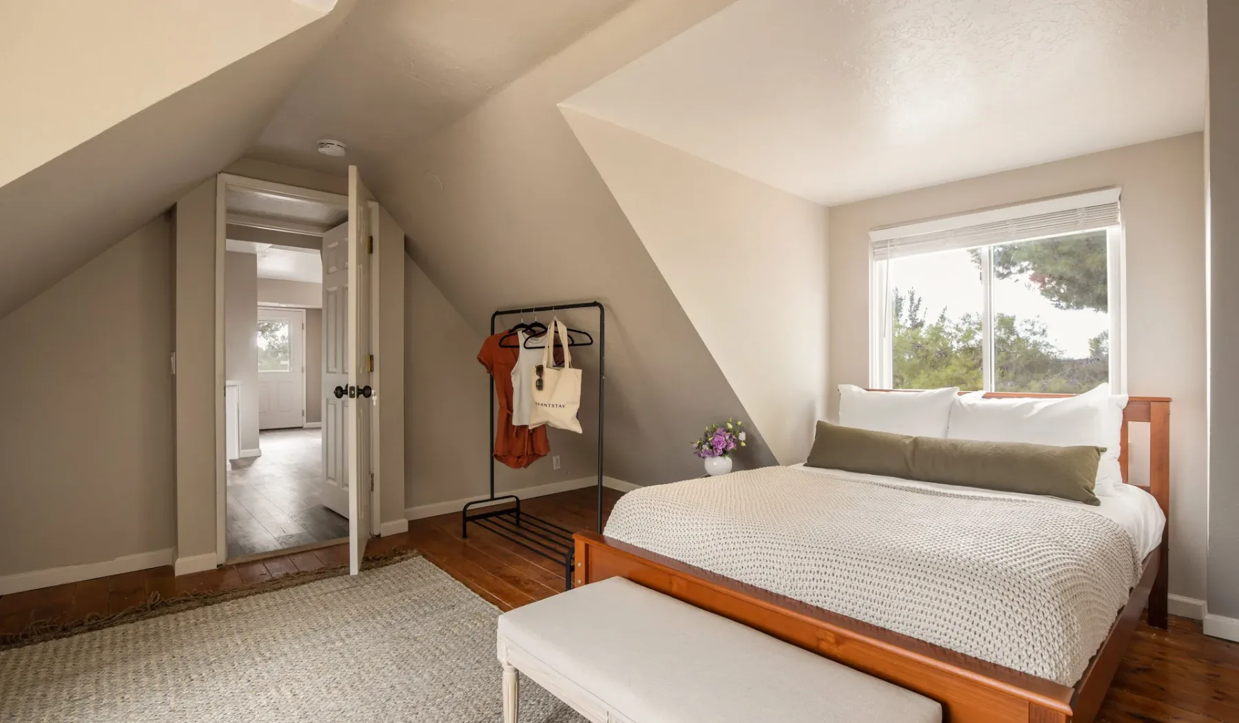 A bright bedroom with a bed beneath a sloped ceiling and a window.
