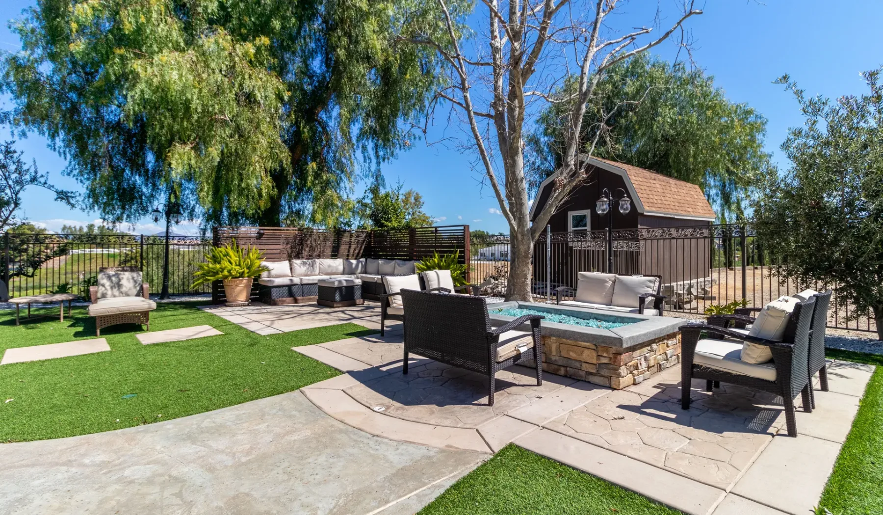 An outdoor patio with cushioned seating, a stone fire pit, and a small shed.