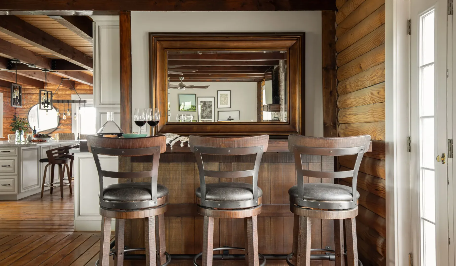 A rustic kitchen and breakfast bar with three stools beneath a large framed mirror.