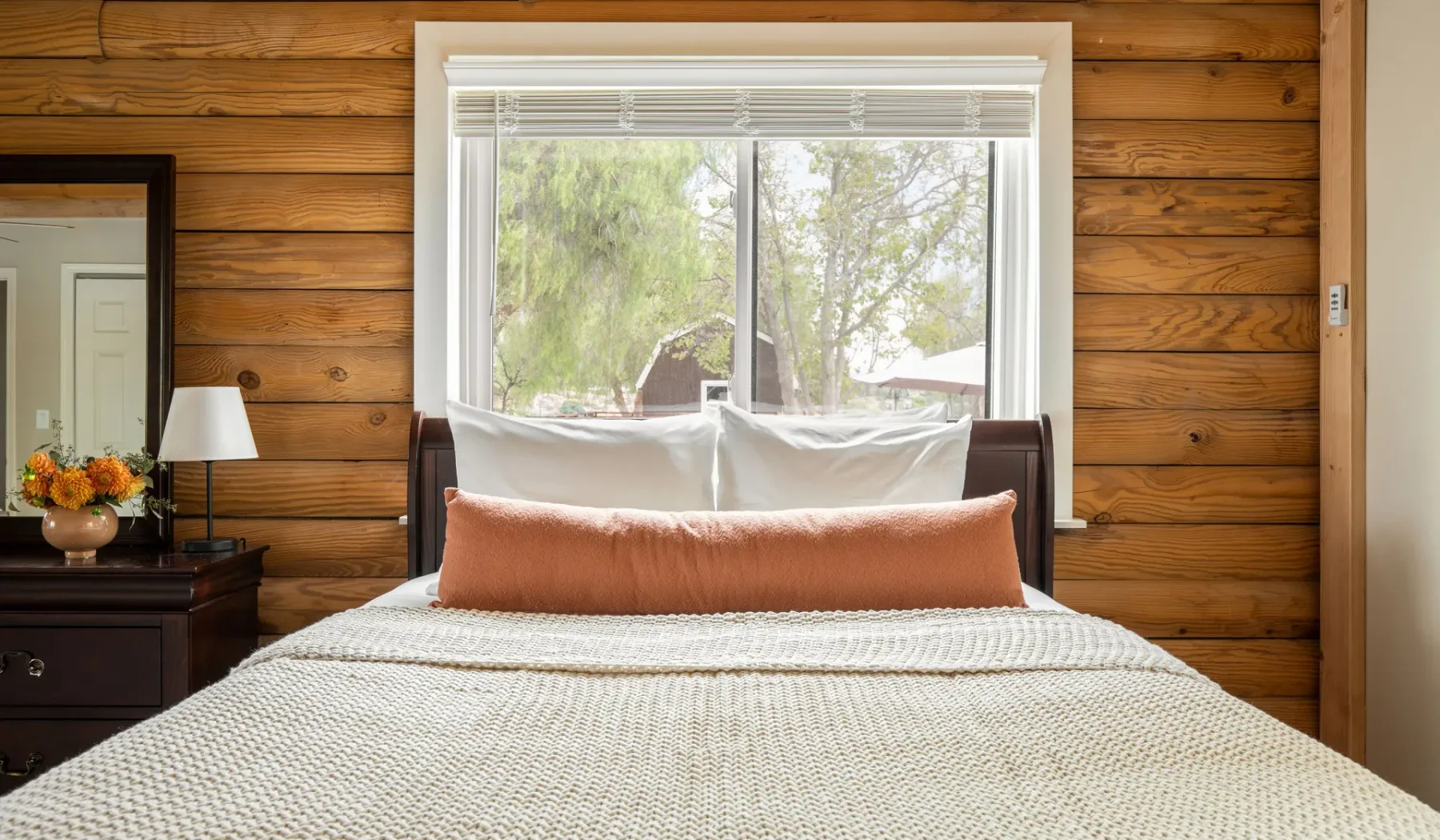 A bedroom with a bed in front of a large window and wood-paneled walls.