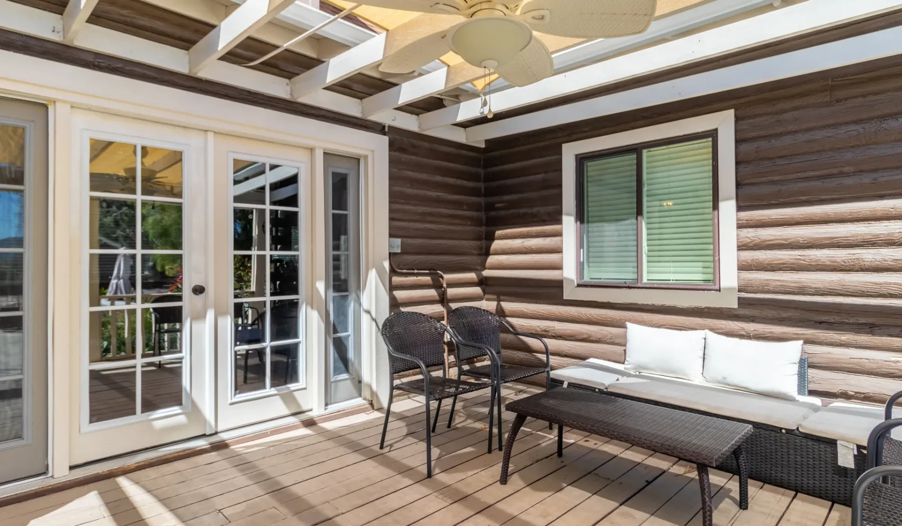A covered wooden deck with outdoor seating beside glass doors.