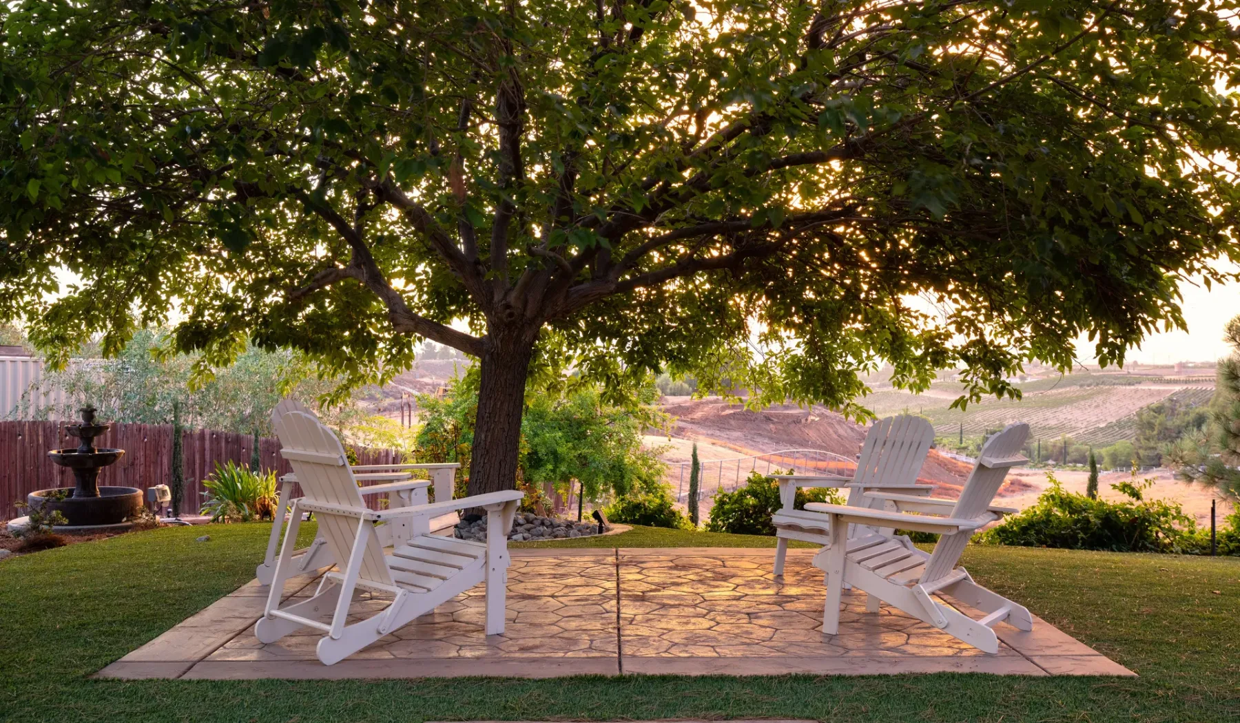 Outdoor seating beneath a broad shade tree, overlooking open fields.