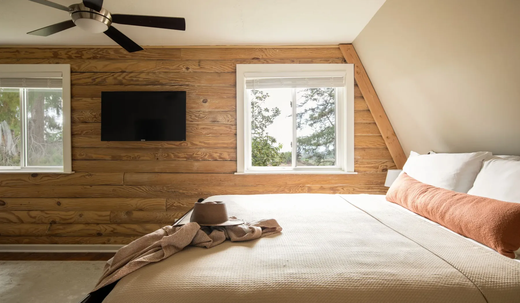 A bedroom with a large bed and a television mounted on the wood-paneled wall.