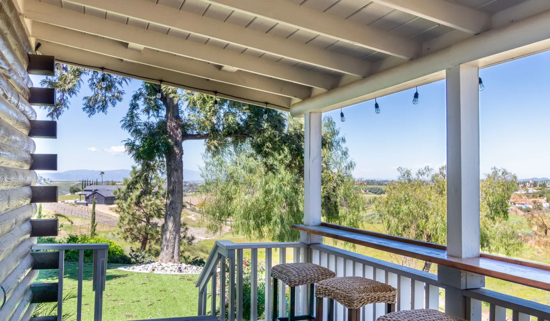 A covered outdoor deck overlooks trees, greenery, and distant homes.