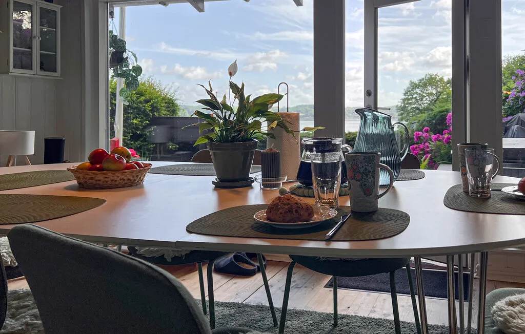 Una mesa de comedor con bebidas y plantas está junto a grandes ventanas con vistas al jardín.