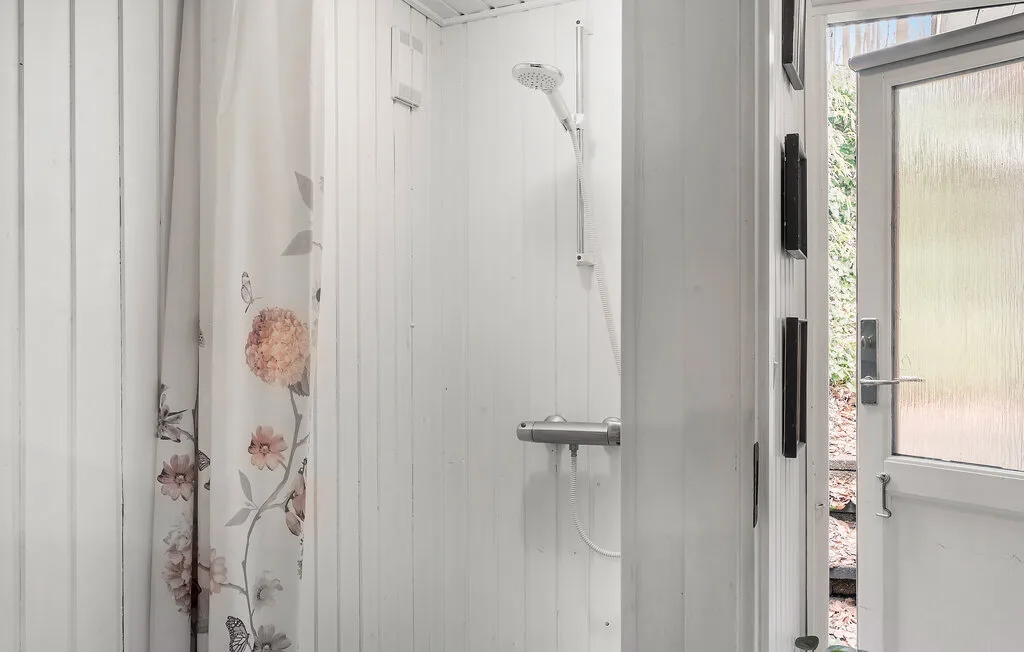 Una ducha blanca con una cortina floral y una puerta abierta.