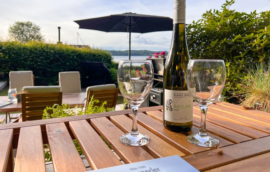 Una mesa de comedor al aire libre está preparada con copas de vino bajo una sombrilla grande.