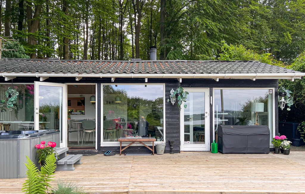 Una casa moderna da a una terraza de madera, con árboles al fondo.
