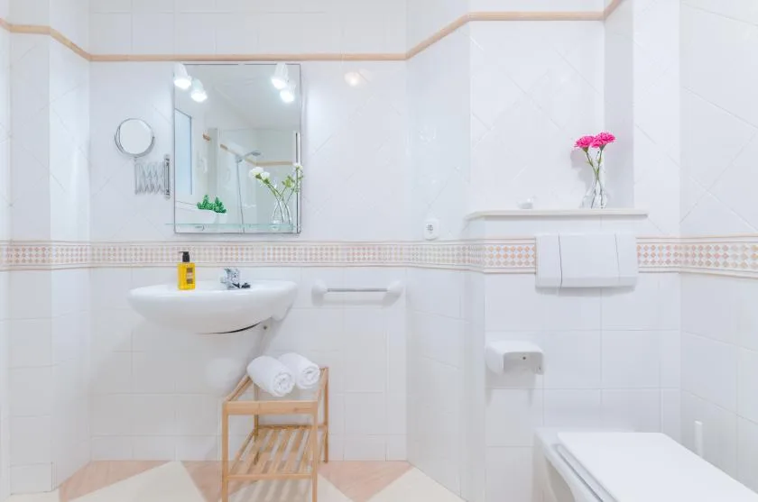Un baño luminoso con azulejos, lavabo suspendido y espejo.