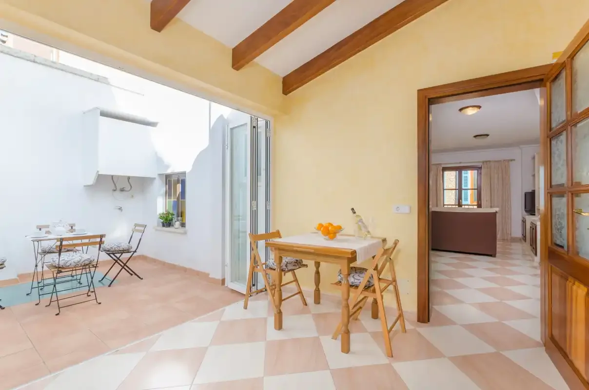 Un comedor luminoso con vigas de madera, una mesa y sillas junto a un patio abierto.