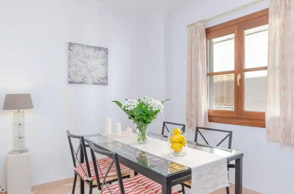 Un comedor luminoso con una mesa de cristal y flores junto a la ventana.