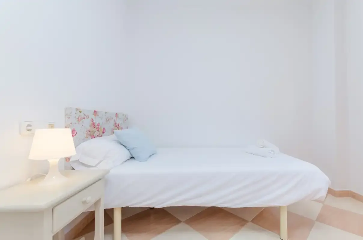 Un dormitorio luminoso con una cama blanca y una lámpara de noche.
