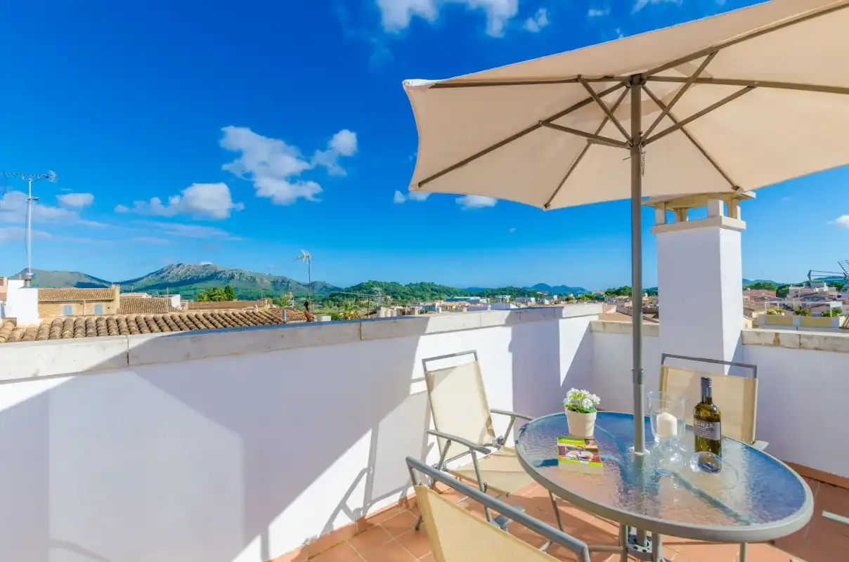 Una terraza en la azotea tiene una mesa y asientos bajo una sombrilla grande.