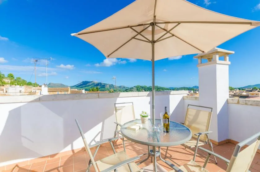 A rooftop terrace with a table and seating beneath a large umbrella.