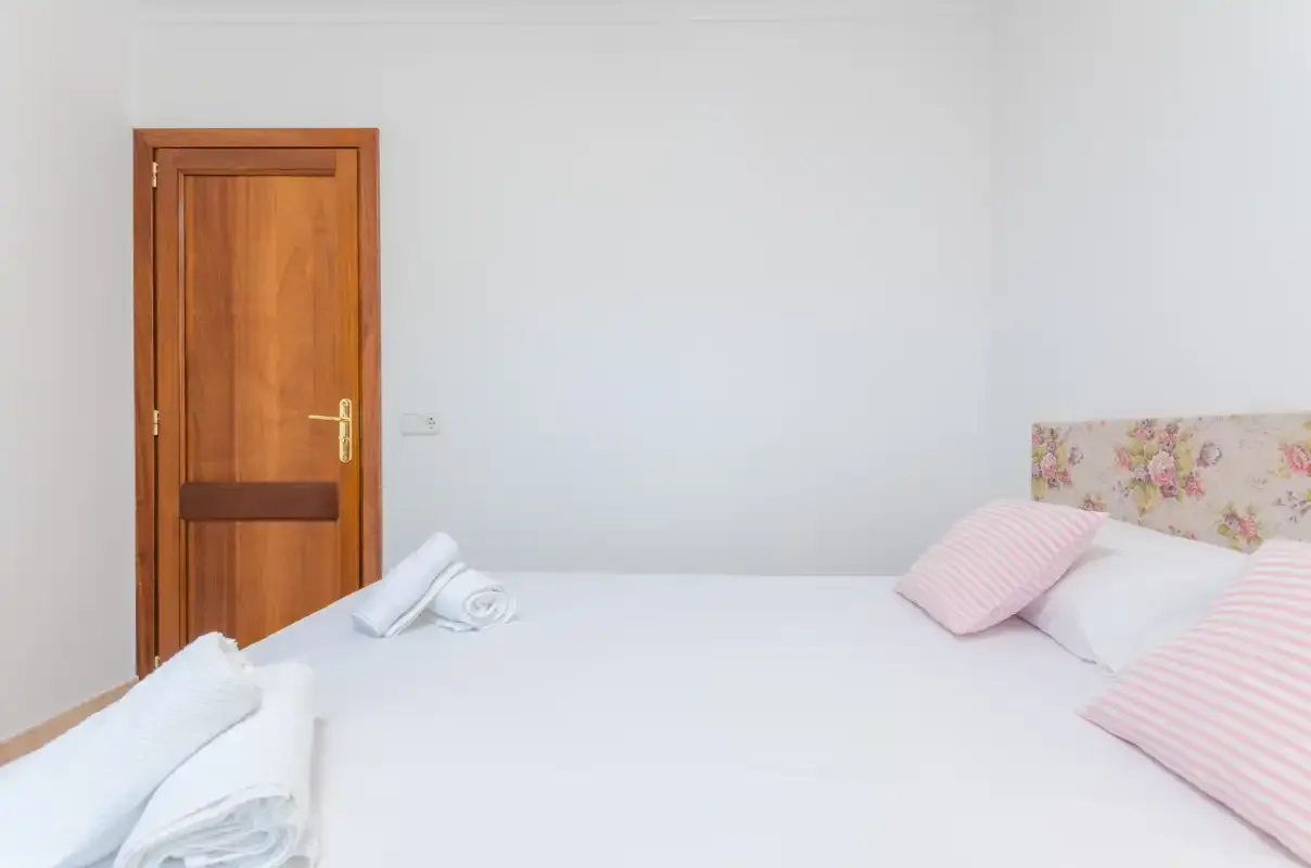Un dormitorio con ropa de cama blanca, cojines a rayas y una puerta de madera.