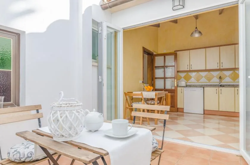 Un comedor da a una cocina con armarios de madera y suelo de baldosas.