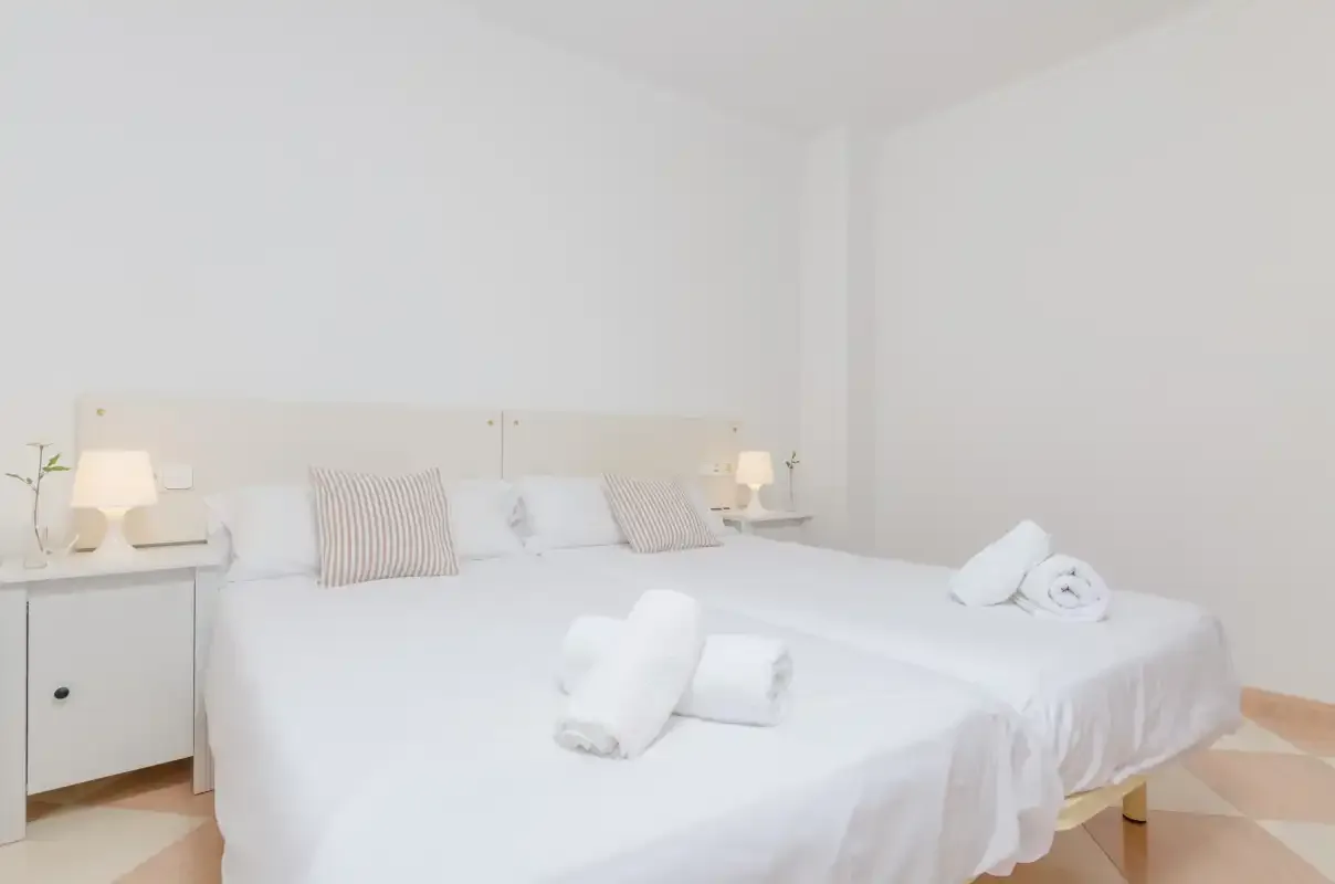 Un dormitorio luminoso con ropa de cama blanca y mesillas de noche.