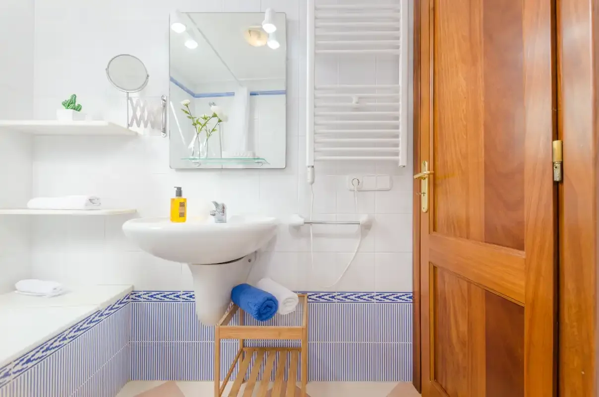 Un baño alicatado con lavabo, espejo y puerta de madera.