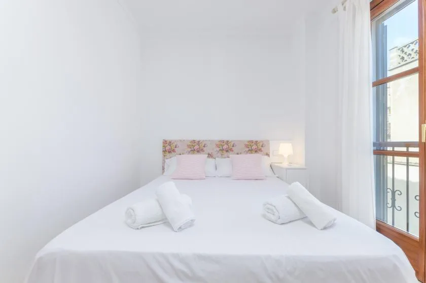 Un dormitorio luminoso con ropa de cama blanca y un cabecero floral.