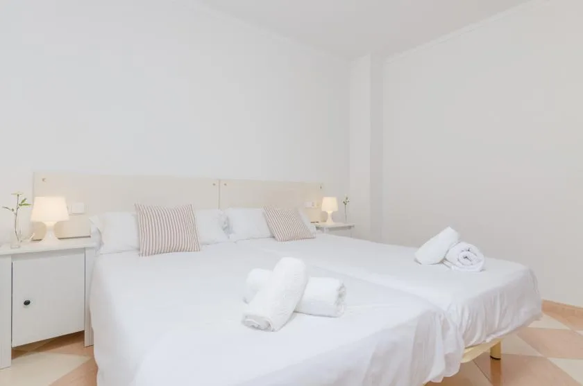 Un dormitorio luminoso con dos camas vestidas de blanco y almohadas a rayas.
