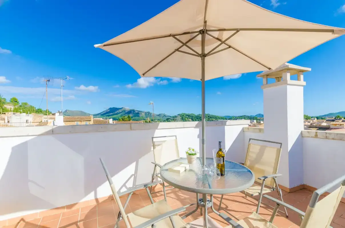 Una terraza en la azotea con una mesa y asientos bajo una sombrilla grande.