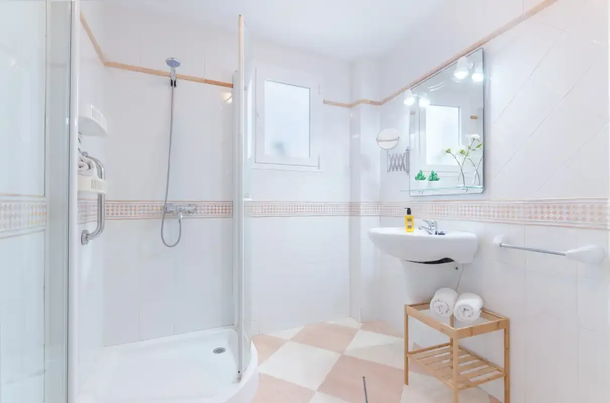 Un baño luminoso con azulejos, ducha, lavabo y espejo.
