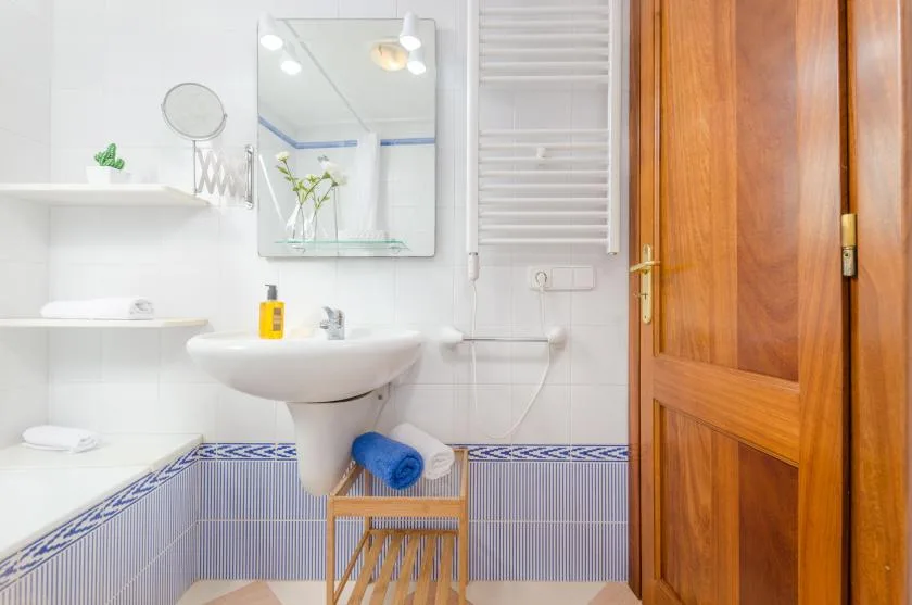 Un baño con lavabo de pared, espejo y puerta de madera.