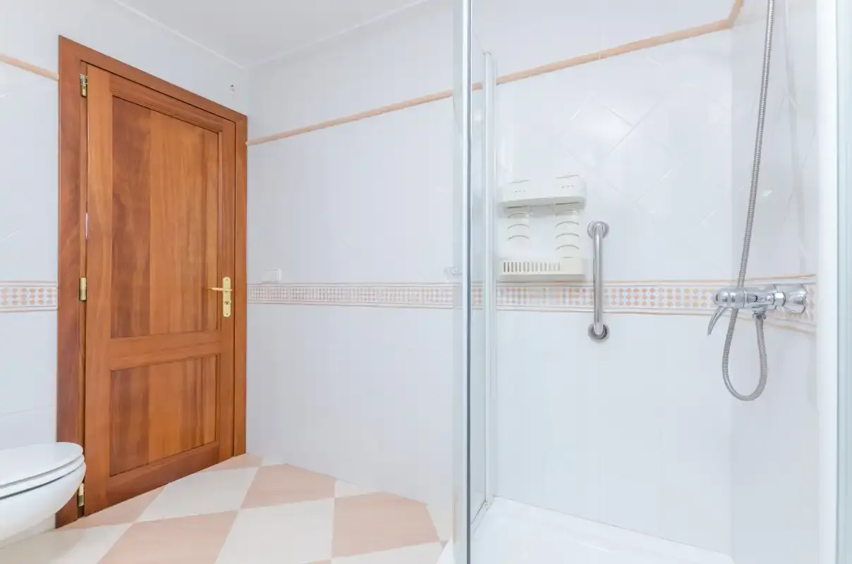 Un baño luminoso con una ducha junto a una puerta de madera.