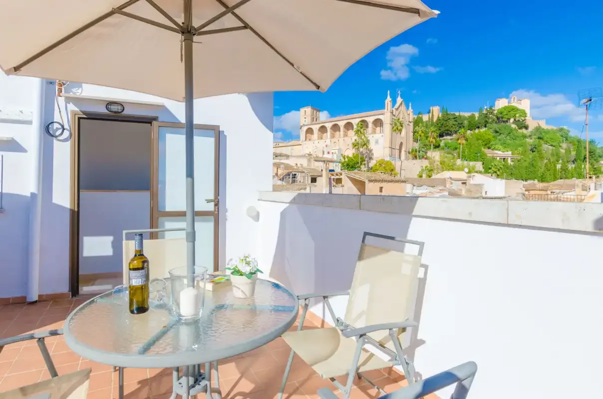 Una zona de estar en una terraza con mesa de vidrio y sombrilla mira hacia edificios históricos.