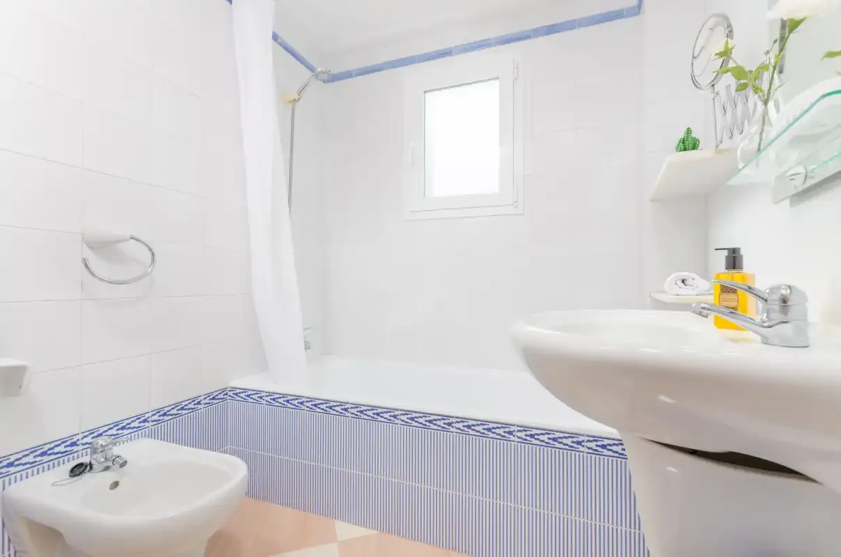 Un baño luminoso con lavabo, bañera y una ventana pequeña.