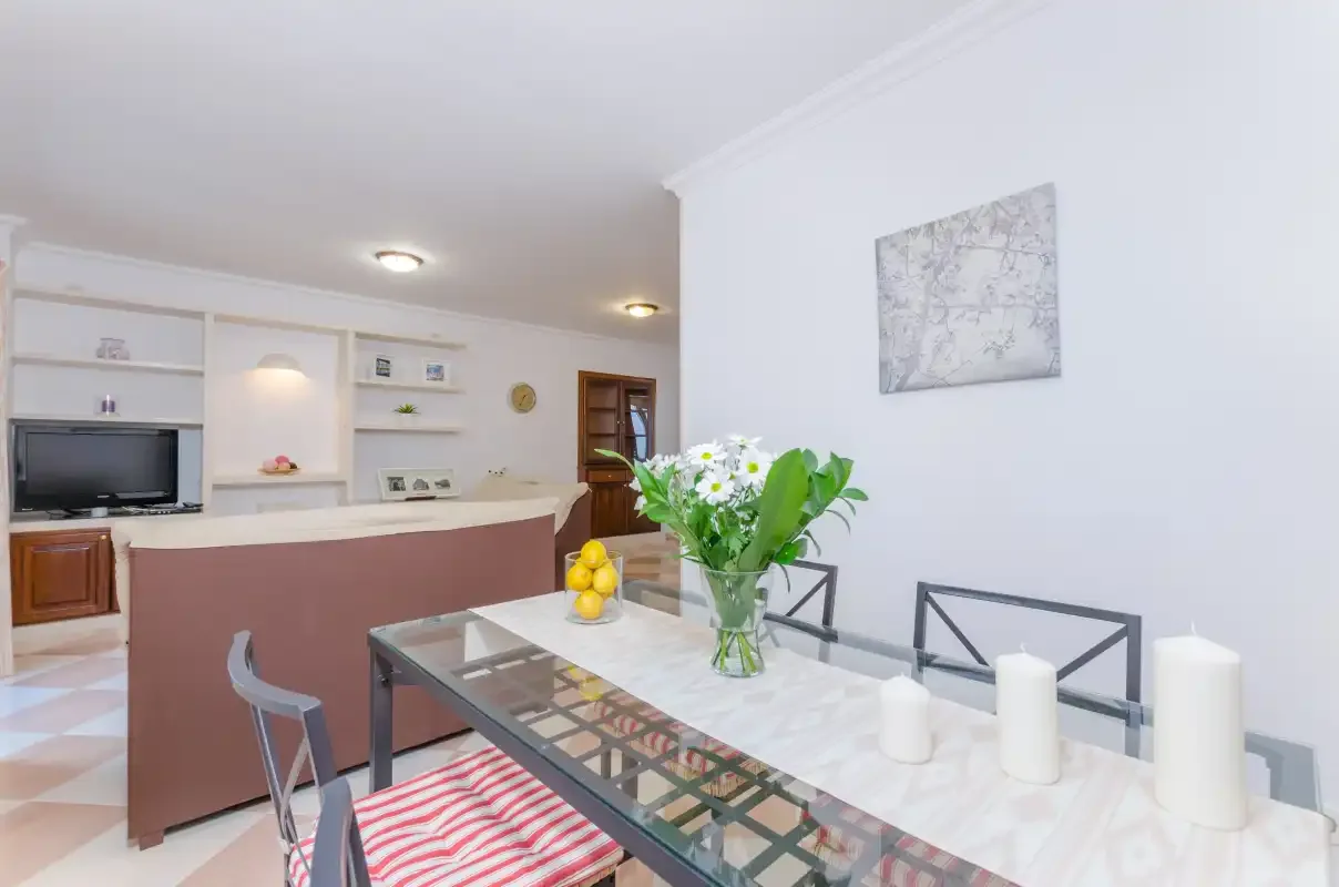 Comedor con mesa de vidrio, flores y una encimera de cocina.