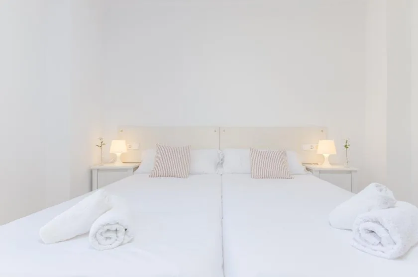 Un dormitorio luminoso con una cama bien tendida y lámparas a ambos lados.