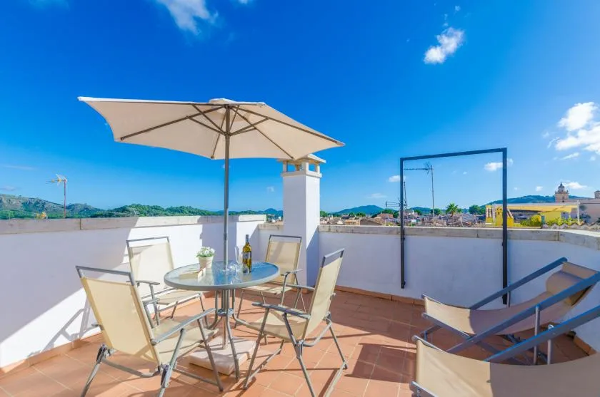Una terraza soleada en la azotea tiene asientos al aire libre bajo una sombrilla grande.