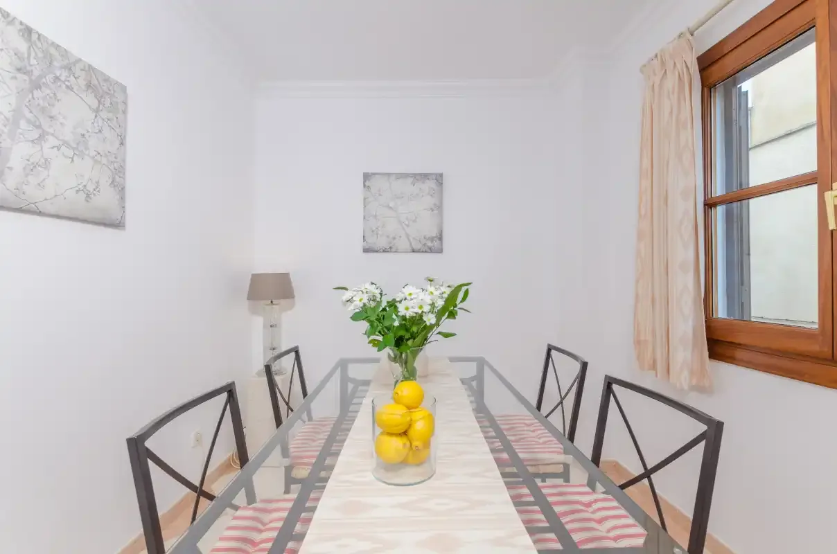 Un comedor con una mesa de cristal, sillas y un jarrón con flores.