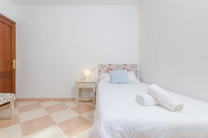 Un dormitorio luminoso con ropa de cama blanca y una mesita de noche.