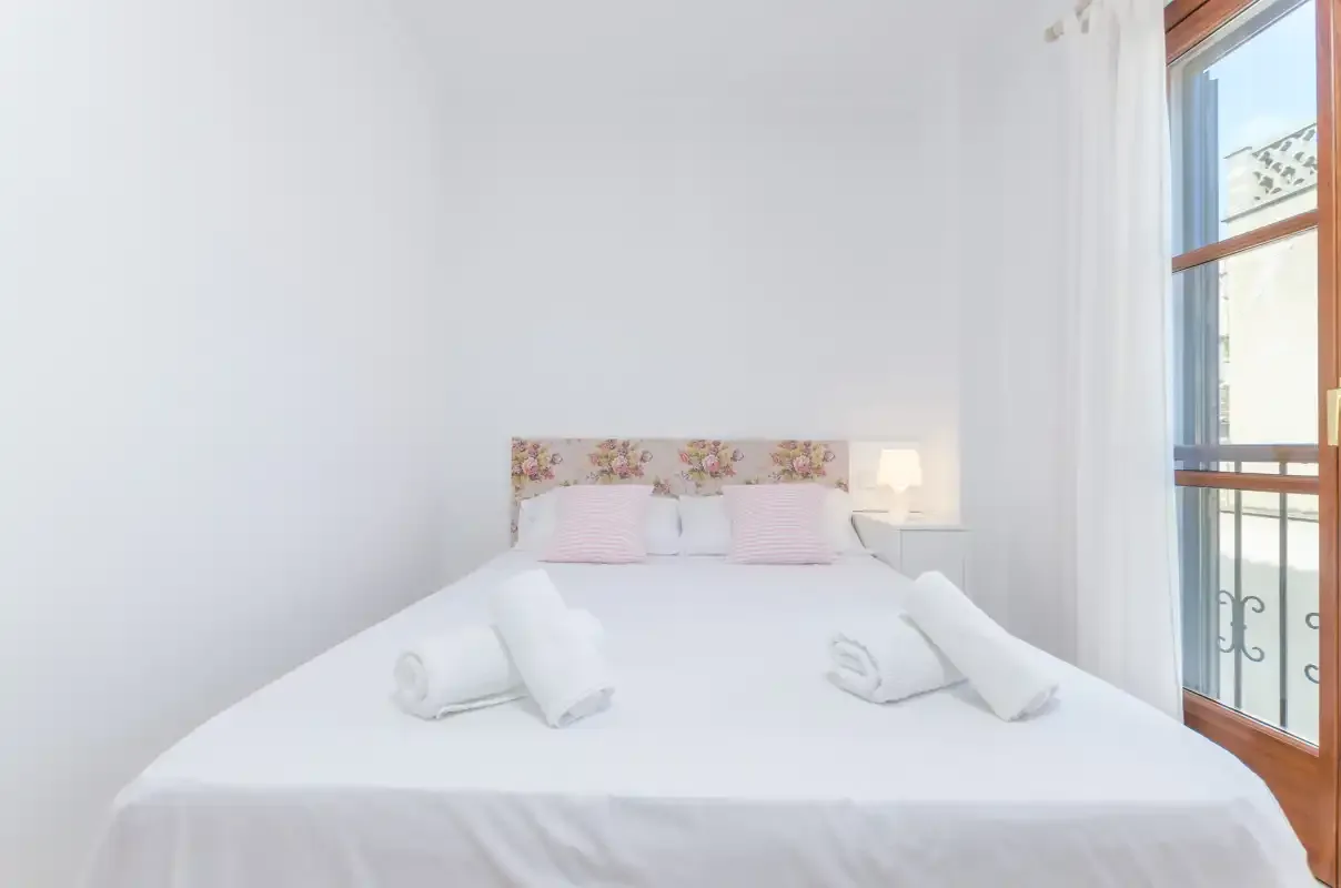 Un dormitorio luminoso con una cama bien tendida y una ventana alta.