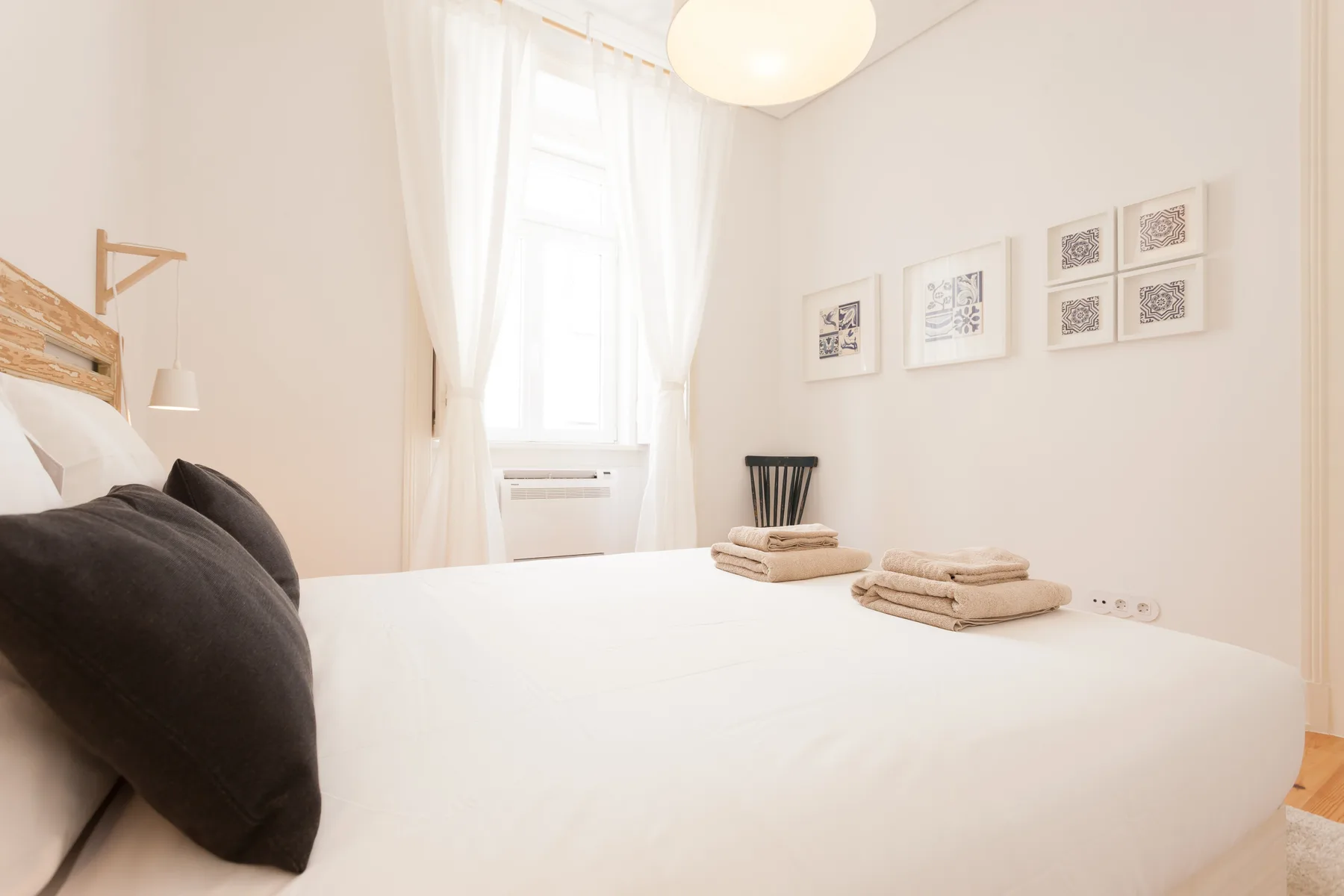 A bright bedroom with a neatly made bed and framed prints on the wall.