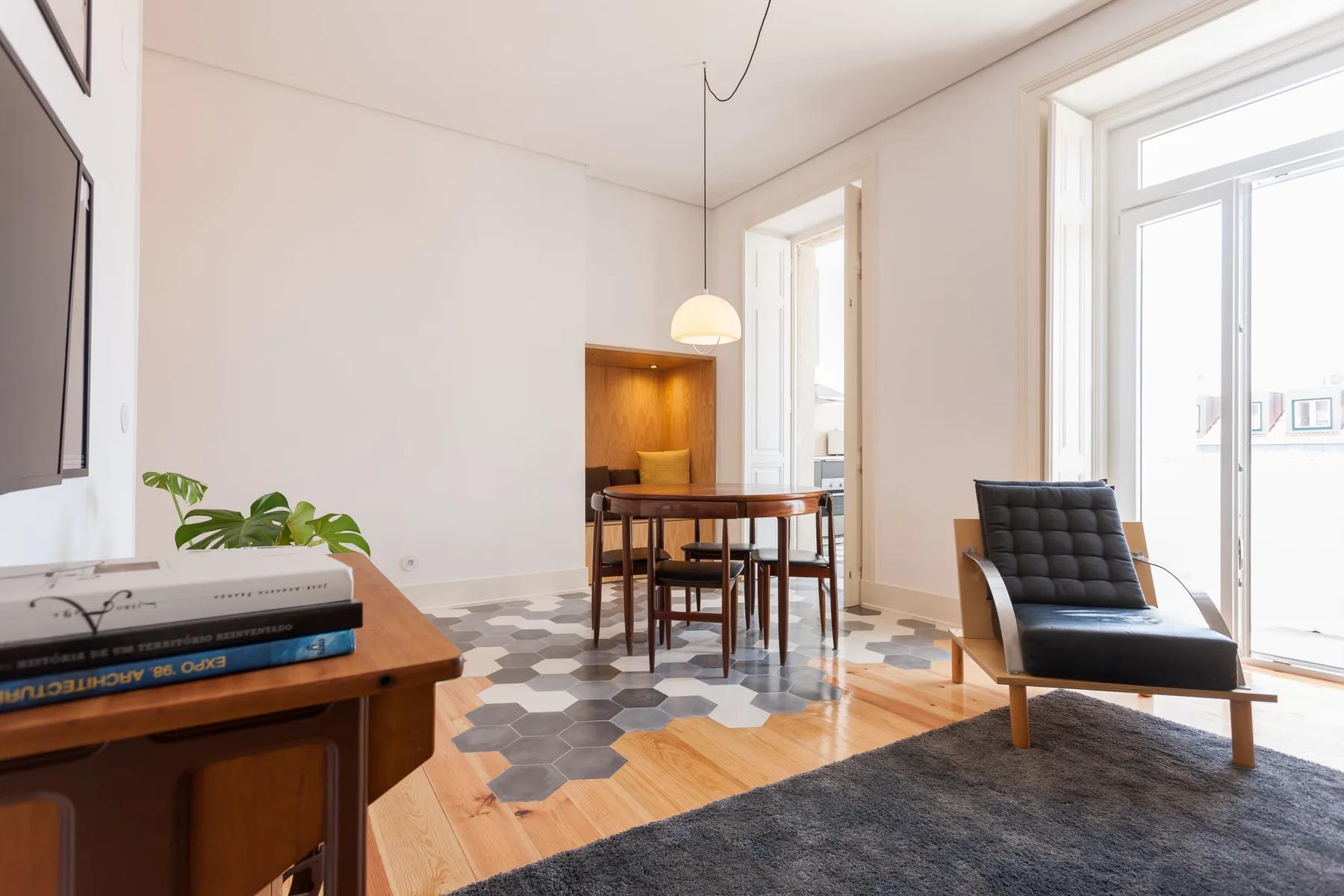 Bright dining and seating area with a wooden table beside tall windows.