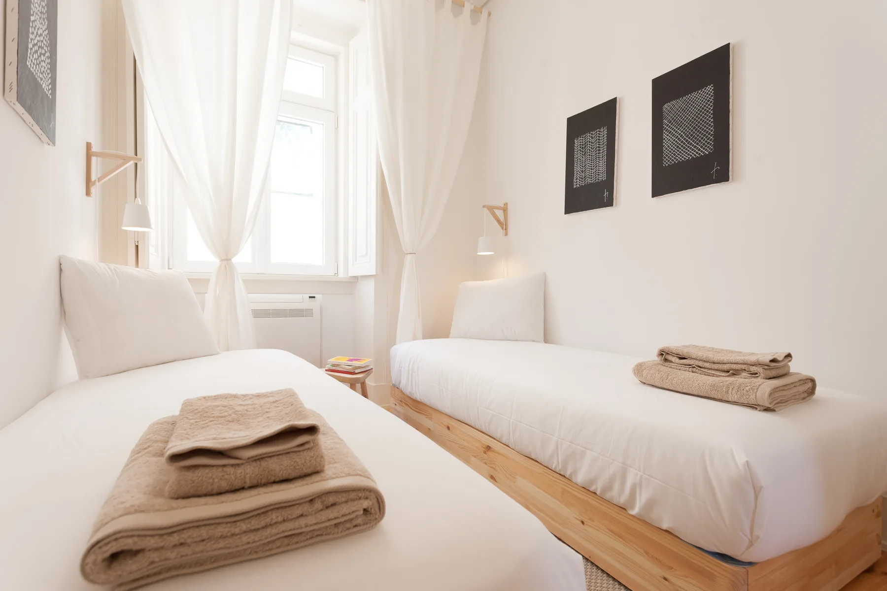 Un dormitorio luminoso con dos camas individuales y cortinas translúcidas junto a la ventana.