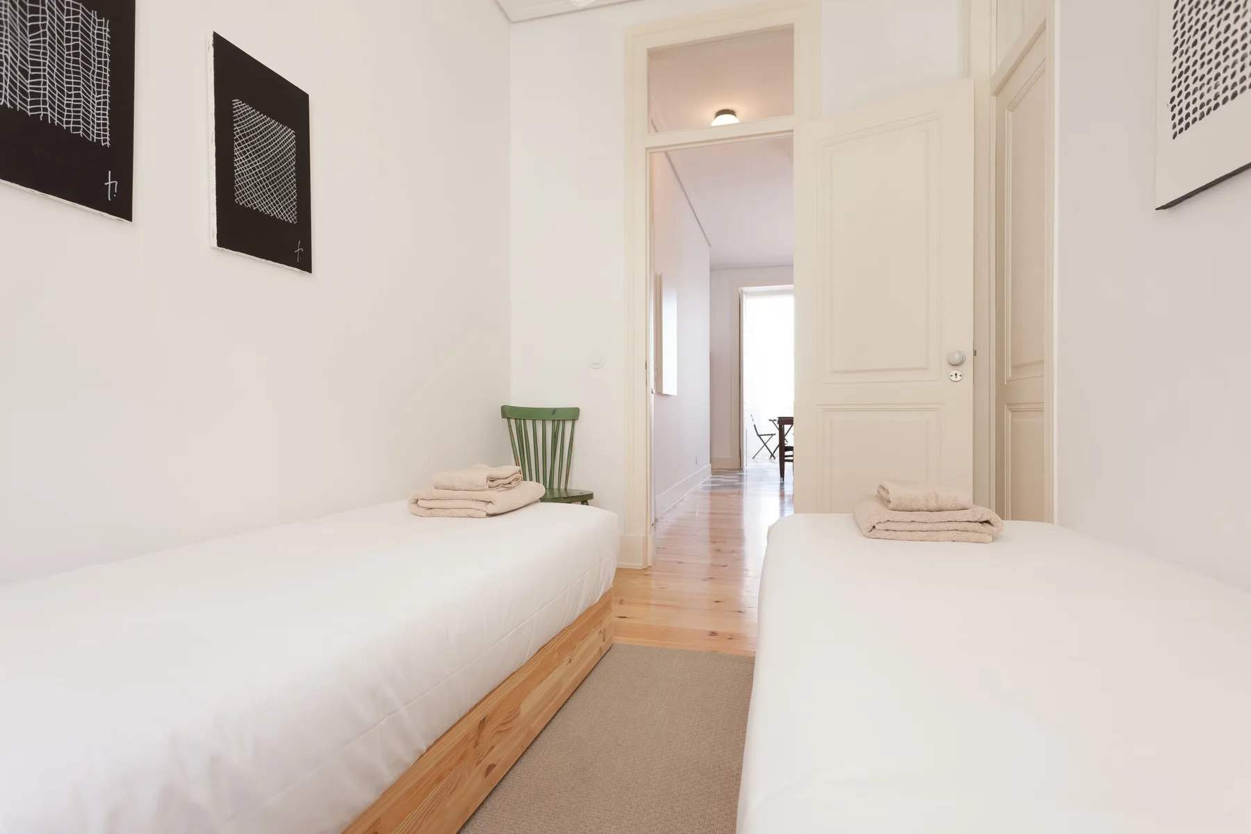 Un dormitorio luminoso con dos camas individuales y una puerta que da a un pasillo.