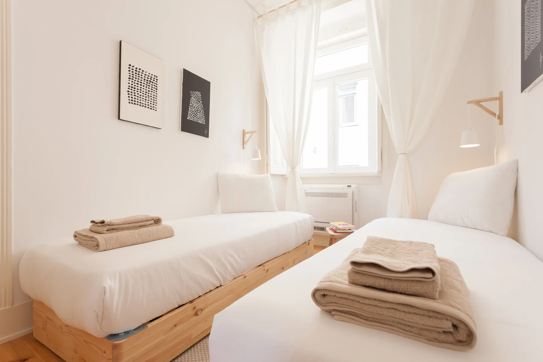 A bright bedroom with two beds and folded towels.