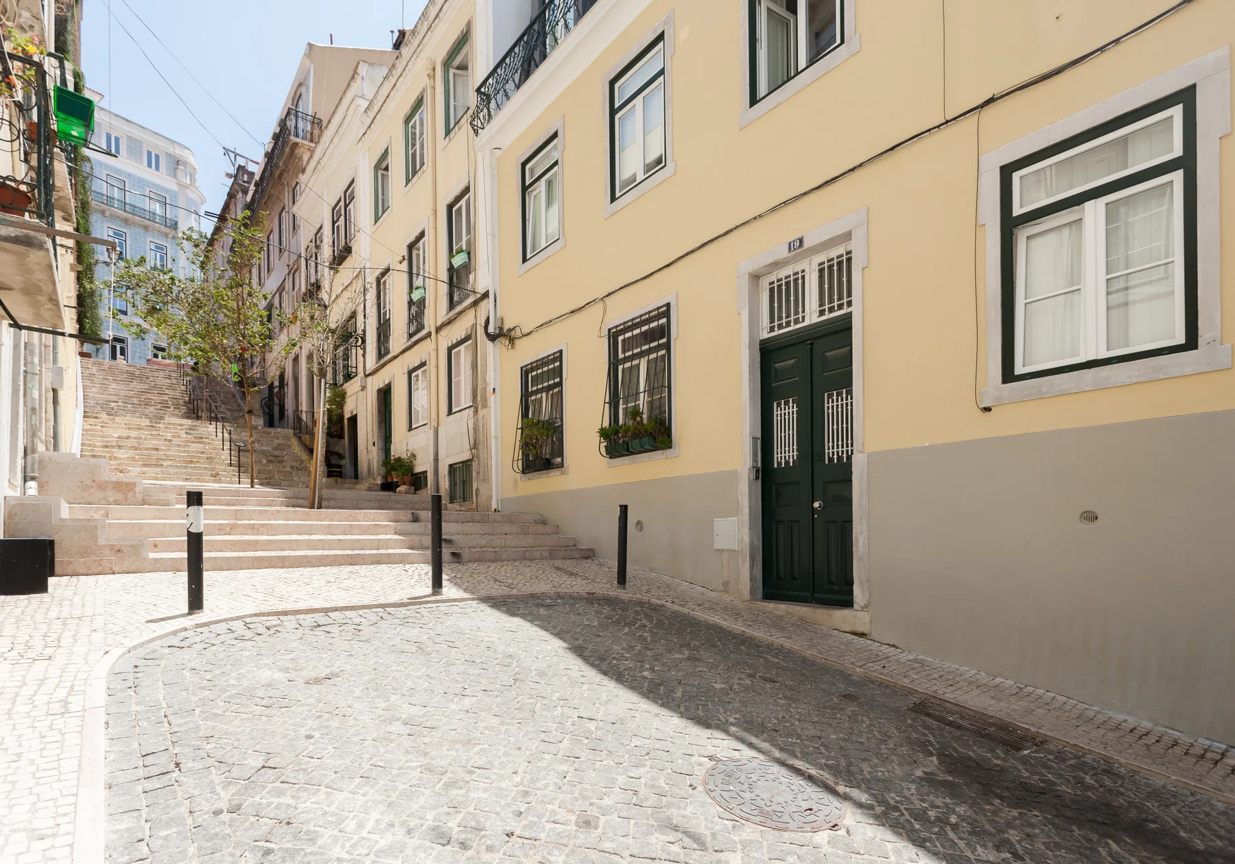 A sunlit cobblestone street runs beside pastel buildings and a flight of steps.