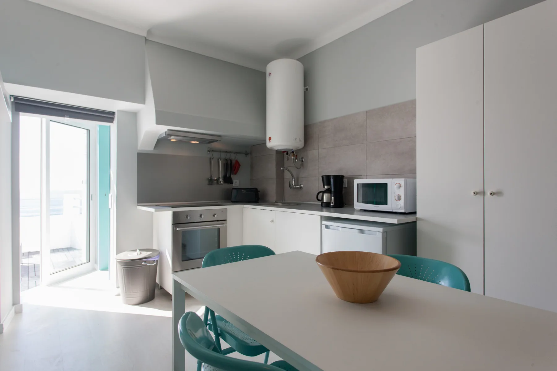 A bright kitchen and dining area with a table, turquoise seating, and cooking appliances.