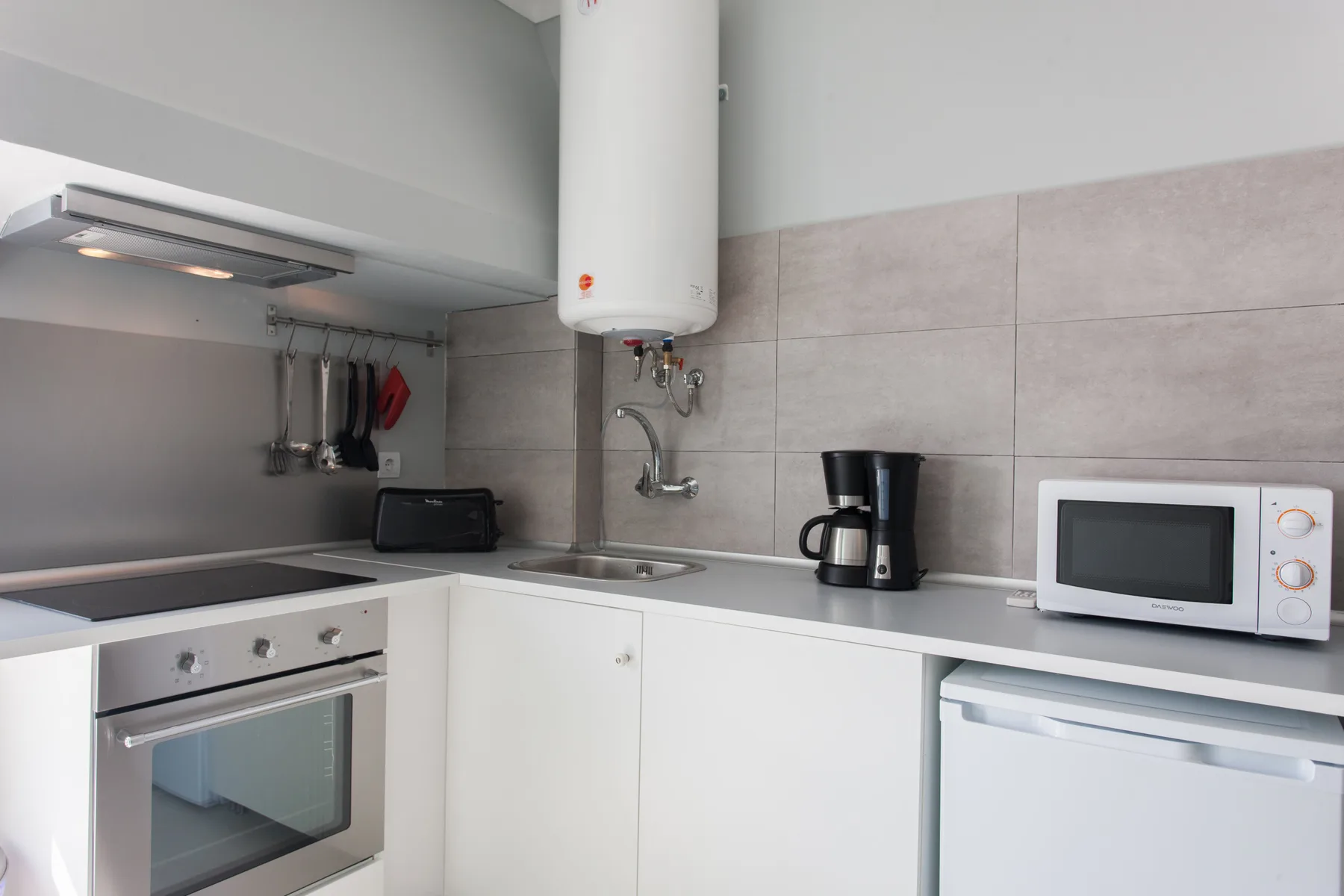 A compact kitchen with a sink, stovetop, microwave, and small appliances.