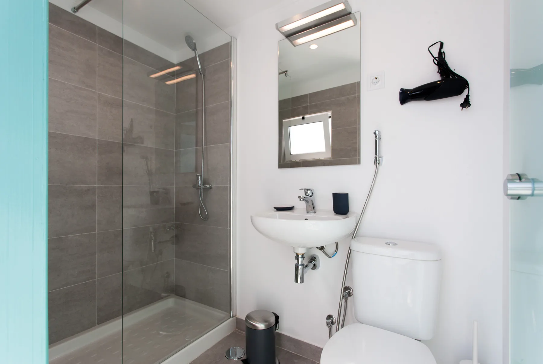 A bathroom with a glass shower, wall-mounted sink, and toilet.
