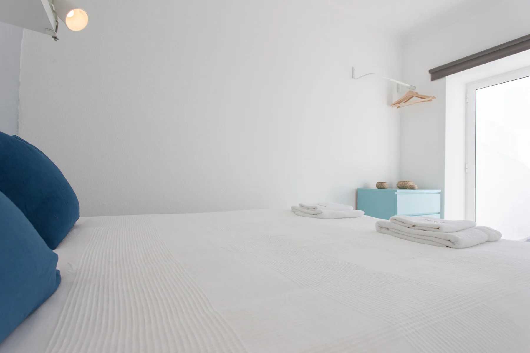 A bright bedroom with a bed, blue pillows, and a small turquoise cabinet.